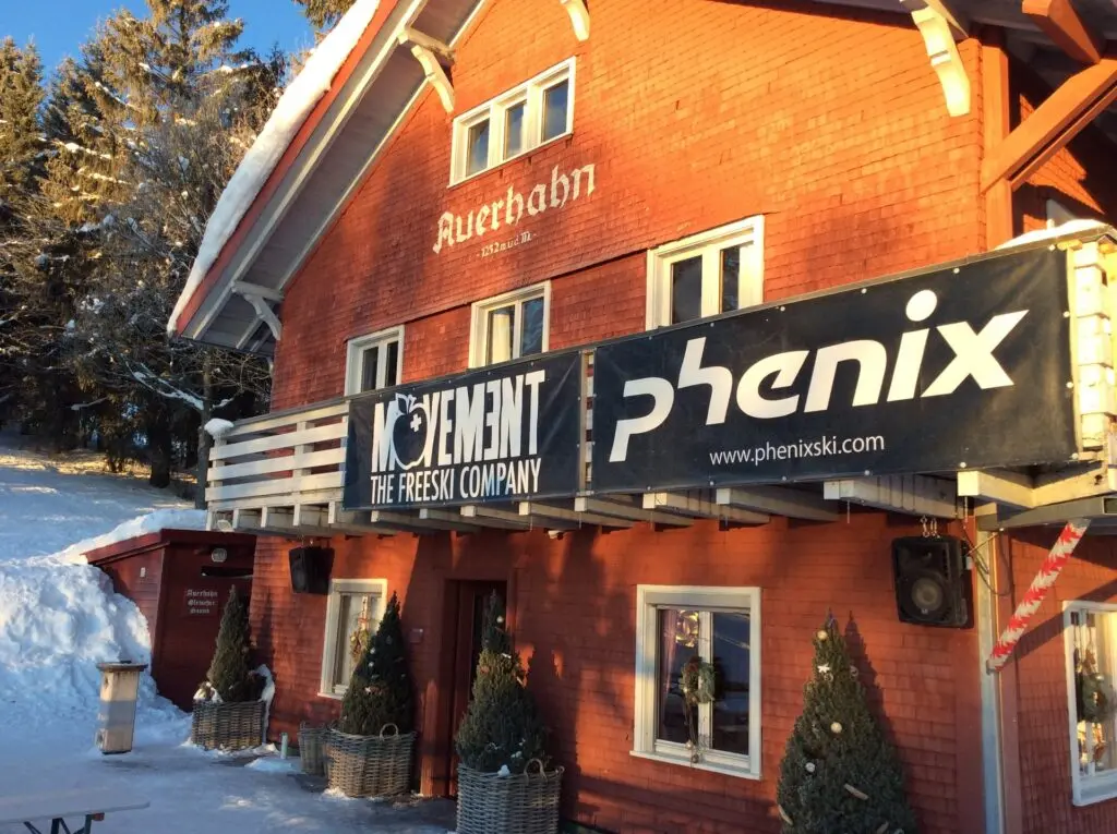 Rotes Holzhaus im Schnee mit Werbebannern „Movement“ und „Phenix“ an der Fassade