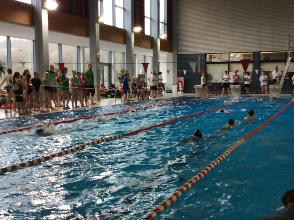 Hallenbad mit Schwimmbahnen während eines Wettkampfs, Zuschauer am Beckenrand