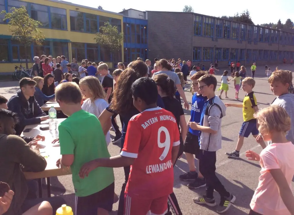 Kinder in Sportkleidung drängen sich an einem Tisch auf dem Schulhof