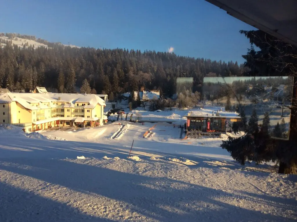 Verschneites Hotel am Waldrand im Abendlicht, davor eine Schneefläche