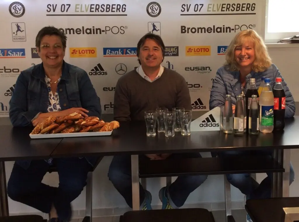 Drei Personen am Tisch vor der Pressewand des SV 07 Elversberg mit Getränken und einem Brezelkorb