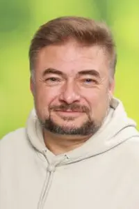 Porträt Thomas Eckert, im hellen Kapuzenpullover vor grünem Hintergrund