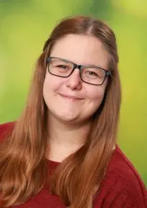 Porträt Saskia Euler, mit langen Haaren und Brille vor grünem Hintergrund