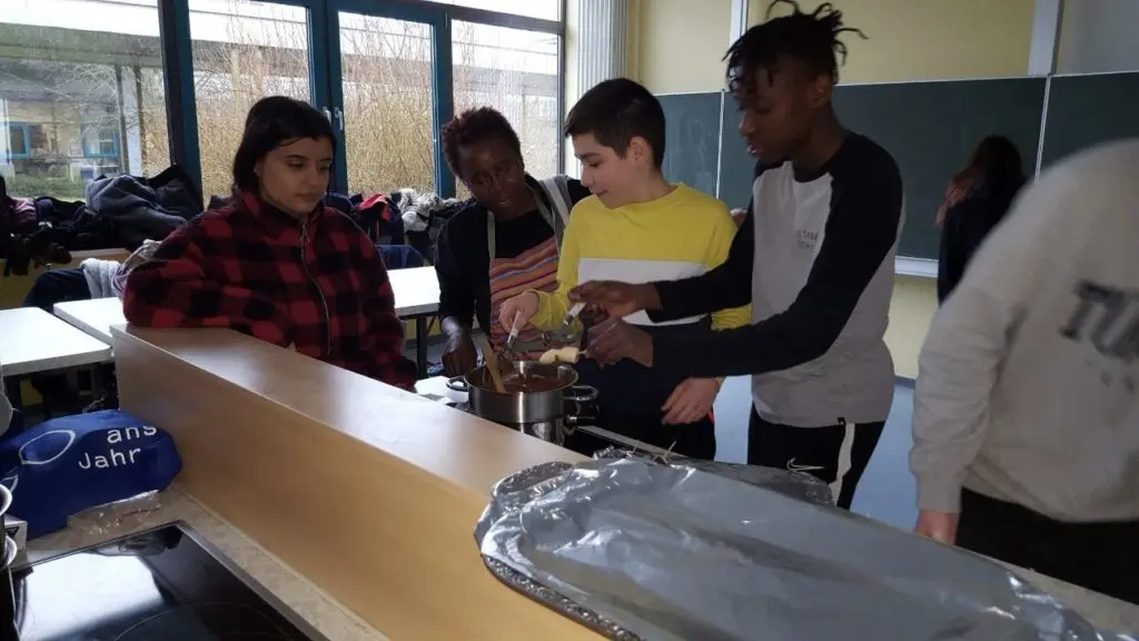 Schülerinnen und Schüler bereiten an der Arbeitsfläche einer Schulküche Speisen zu