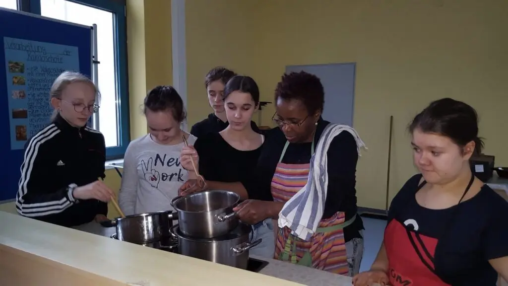 Schülerinnen mit Schürzen kochen gemeinsam an Töpfen in einer Schulküche