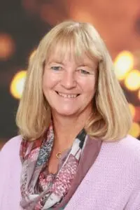 Porträt Annette Frisch, mit blonden Haaren und Schal vor Hintergrund mit Lichterpunkten