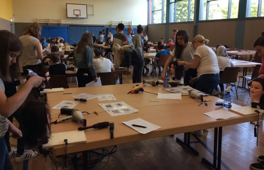 Schülerinnen und Schüler an Werkstationen mit Arbeitsmaterial in einer Sporthalle