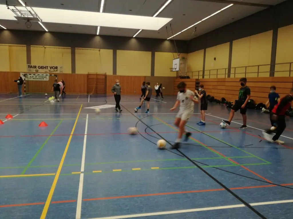 Kinder spielen in der Fußball-AG mit Bällen in einer Sporthalle mit blauem Boden