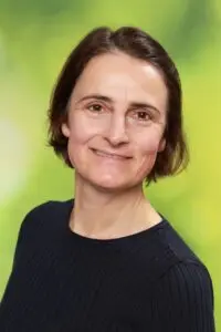 Porträt Isabell Göttert, mit kurzen dunklen Haaren im schwarzen Oberteil vor grünem Hintergrund