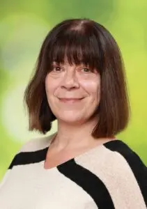 Porträt Melanie Gottschall, mit dunklem Pony und gestreiftem Pullover vor grünem Hintergrund