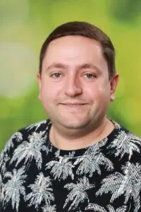 Porträt Julian Graus, im gemusterten schwarzen Hemd vor grünem Hintergrund