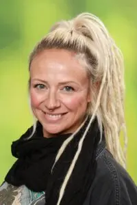 Porträt Vera Hahnen, mit blonden Dreadlocks und schwarzem Schal vor grünem Hintergrund