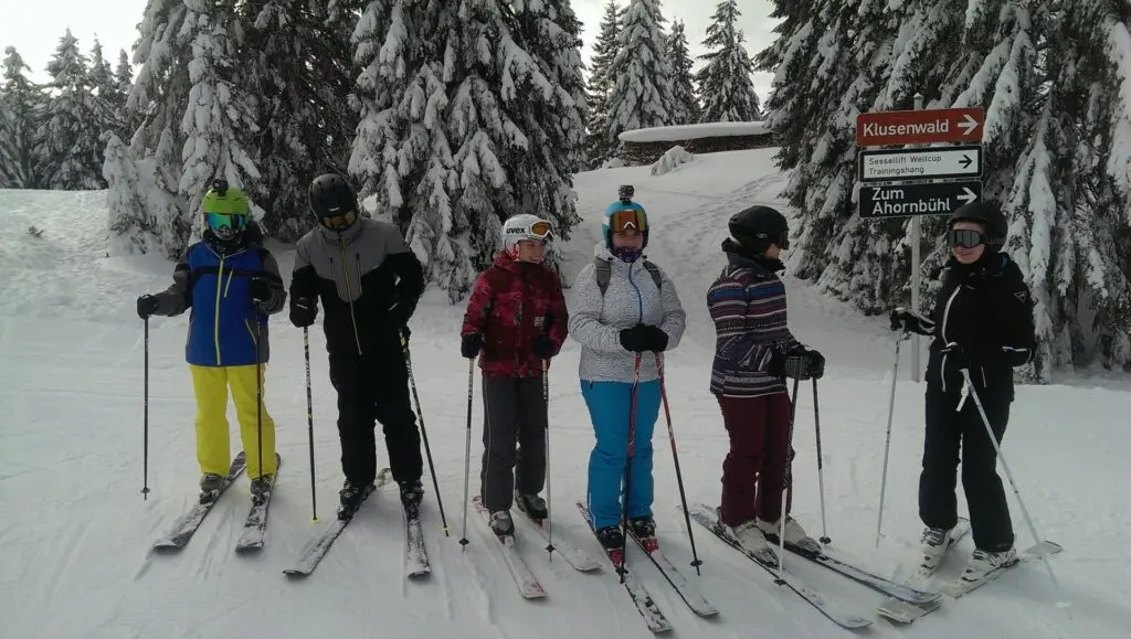 Skifahrergruppe steht nebeneinander auf einer Piste vor verschneiten Tannen
