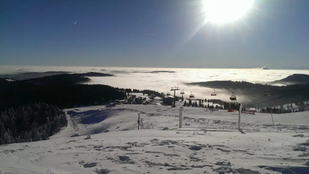 Sonne über verschneiter Berglandschaft mit Nebel in den Tälern, Blick von der Piste
