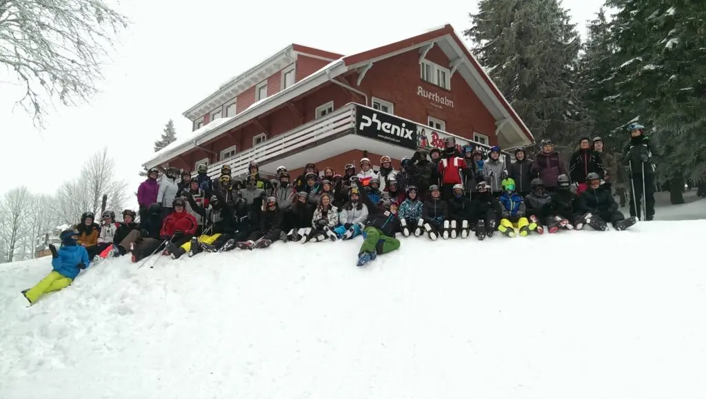 Große Gruppe Jugendlicher sitzt und liegt im Schnee vor einer Berghütte