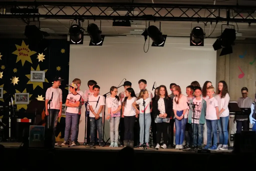 Schülerchor in bunten T-Shirts steht auf einer beleuchteten Bühne mit Sternendekoration