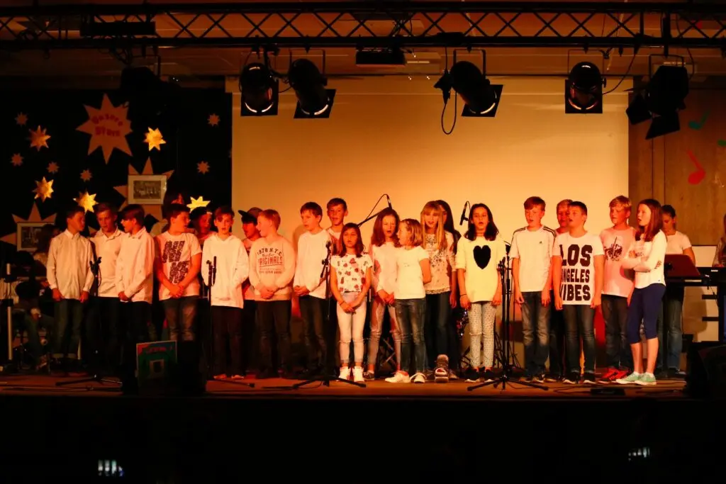 Große Gruppe Schülerinnen und Schüler singt in einer Reihe auf der Bühne der Aula