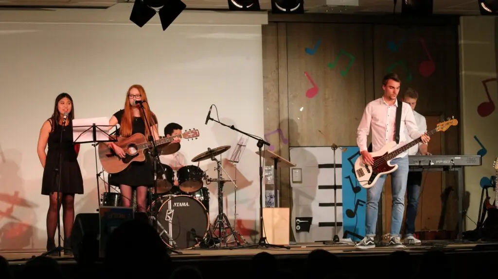 Schülerband mit Sängerinnen, Gitarren, Bass und Schlagzeug musiziert auf der Bühne