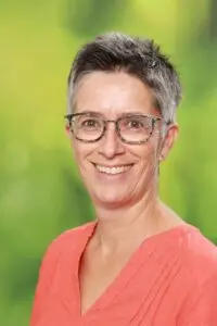 Porträt Ruth Jäckel, mit kurzen grauen Haaren und Brille vor grünem Hintergrund