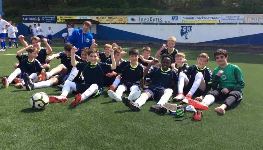 Schülerfußballmannschaft sitzt mit Bällen auf dem Rasen für ein Mannschaftsfoto