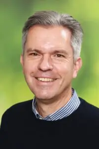 Porträt Bruno Kistner, im dunklen Pullover mit Hemdkragen vor grünem Hintergrund