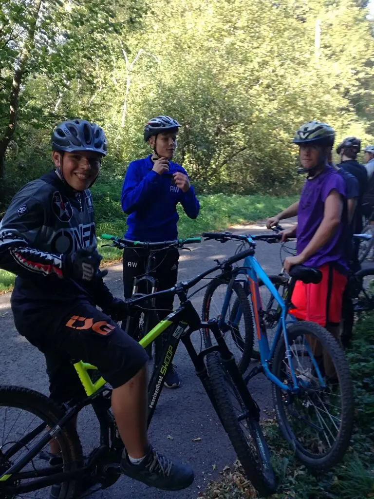 Drei Jugendliche mit Helm und Mountainbikes stehen nebeneinander am Waldrand
