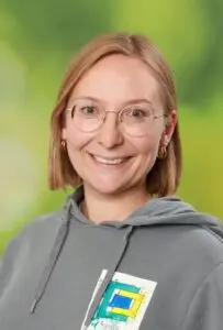 Porträt Lisa Kron, mit Brille im grauen Kapuzenpullover vor grünem Hintergrund