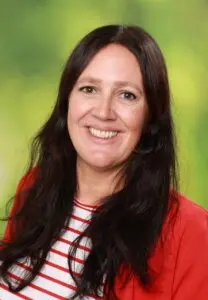 Porträt Kerstin Kuhn, mit langen dunklen Haaren und roter Jacke vor grünem Hintergrund
