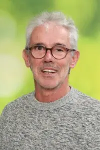 Porträt Peter Lichtental, mit grauen Haaren und Brille vor grünem Hintergrund