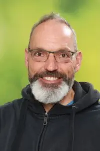 Porträt Markus Mörsdorf, mit grauem Bart und Brille vor grünem Hintergrund