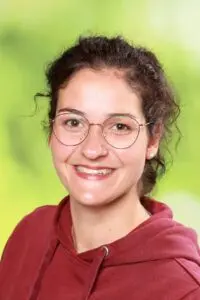 Porträt Jessica Müller, mit Brille im roten Kapuzenpullover vor grünem Hintergrund
