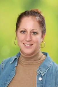 Porträt Elke Prinz, mit hochgesteckten Haaren und Jeansjacke vor grünem Hintergrund