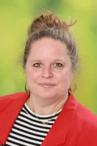 Porträt Kathrin Rauber, mit Haarknoten und roter Jacke vor grünem Hintergrund
