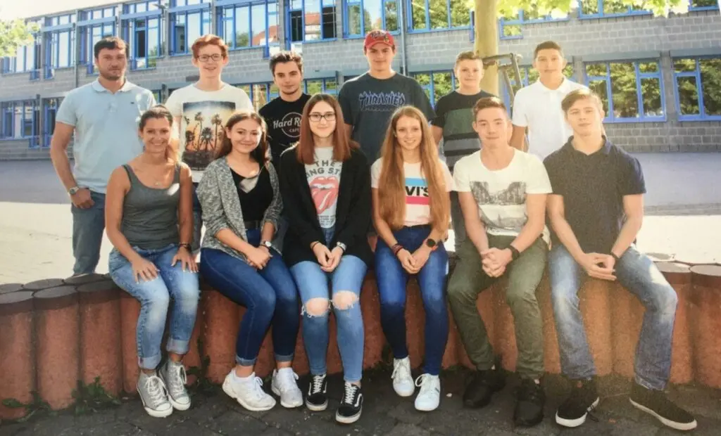 Gruppenfoto der Schülervertretung: Jugendliche sitzen und stehen im Freien vor dem Schulgebäude