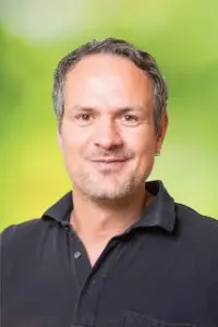 Porträt Christian Sahl, im dunklen Poloshirt vor grünem Hintergrund