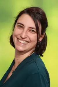 Porträt Brigitta Scheid, mit dunklen Haaren im grünen Oberteil vor grünem Hintergrund