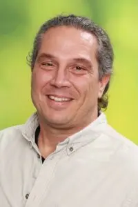Porträt Christian Schmeer, lächelnd im hellen Hemd vor grünem Hintergrund