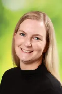 Porträt Lisa Schmidt, mit blonden Haaren im schwarzen Oberteil vor grünem Hintergrund