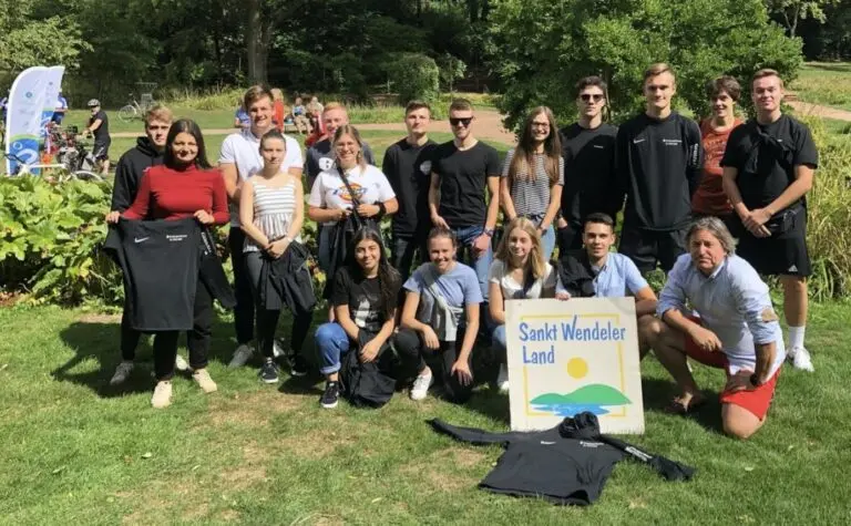 Gruppe Jugendlicher und Erwachsener posiert im Grünen mit einem Schild zur Aktion Schulradeln
