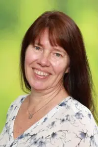 Porträt Diane Spanier, mit langen dunklen Haaren und geblümter Bluse vor grünem Hintergrund
