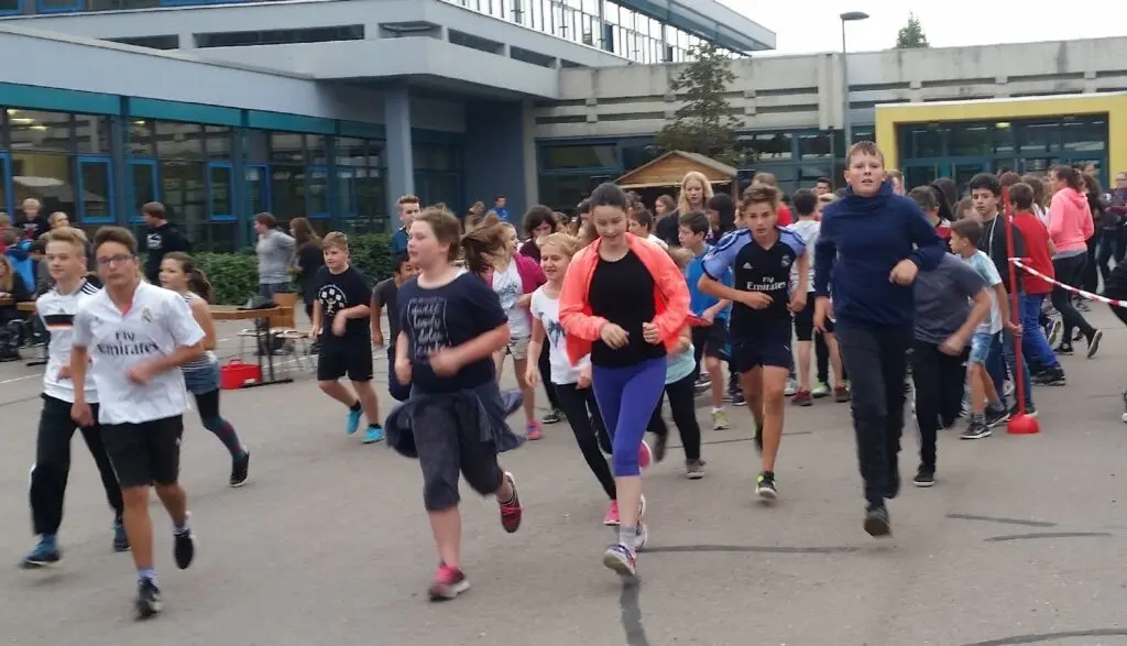 Schülerinnen und Schüler laufen in einer Gruppe über den Schulhof beim Spendenlauf