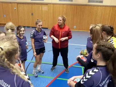 Schülerinnen-Team steht in der Sporthalle im Kreis um eine Trainerin in Rot