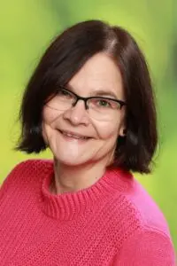 Porträt Andrea Wagner, mit Brille im pinkfarbenen Pullover vor grünem Hintergrund