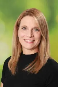 Porträt Eva Wagner, mit langen Haaren im schwarzen Oberteil vor grünem Hintergrund