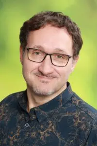 Porträt Björn Werner, mit Brille im gemusterten Hemd vor grünem Hintergrund