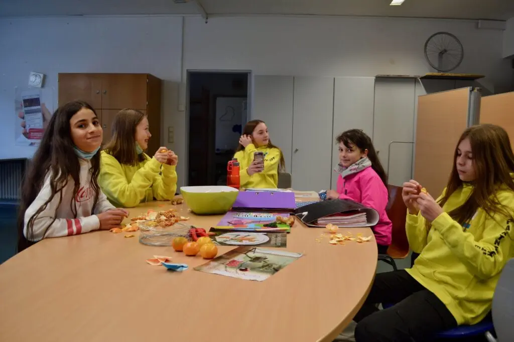 Schülerinnen in gelben T-Shirts sitzen in der Zaire-AG an einem Tisch mit Obst und Essen im Klassenraum