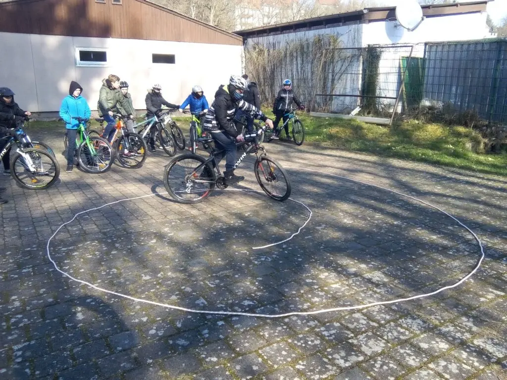 Schülergruppe mit Fahrrädern und Helmen auf dem Schulhof an einem aufgemalten Kreis